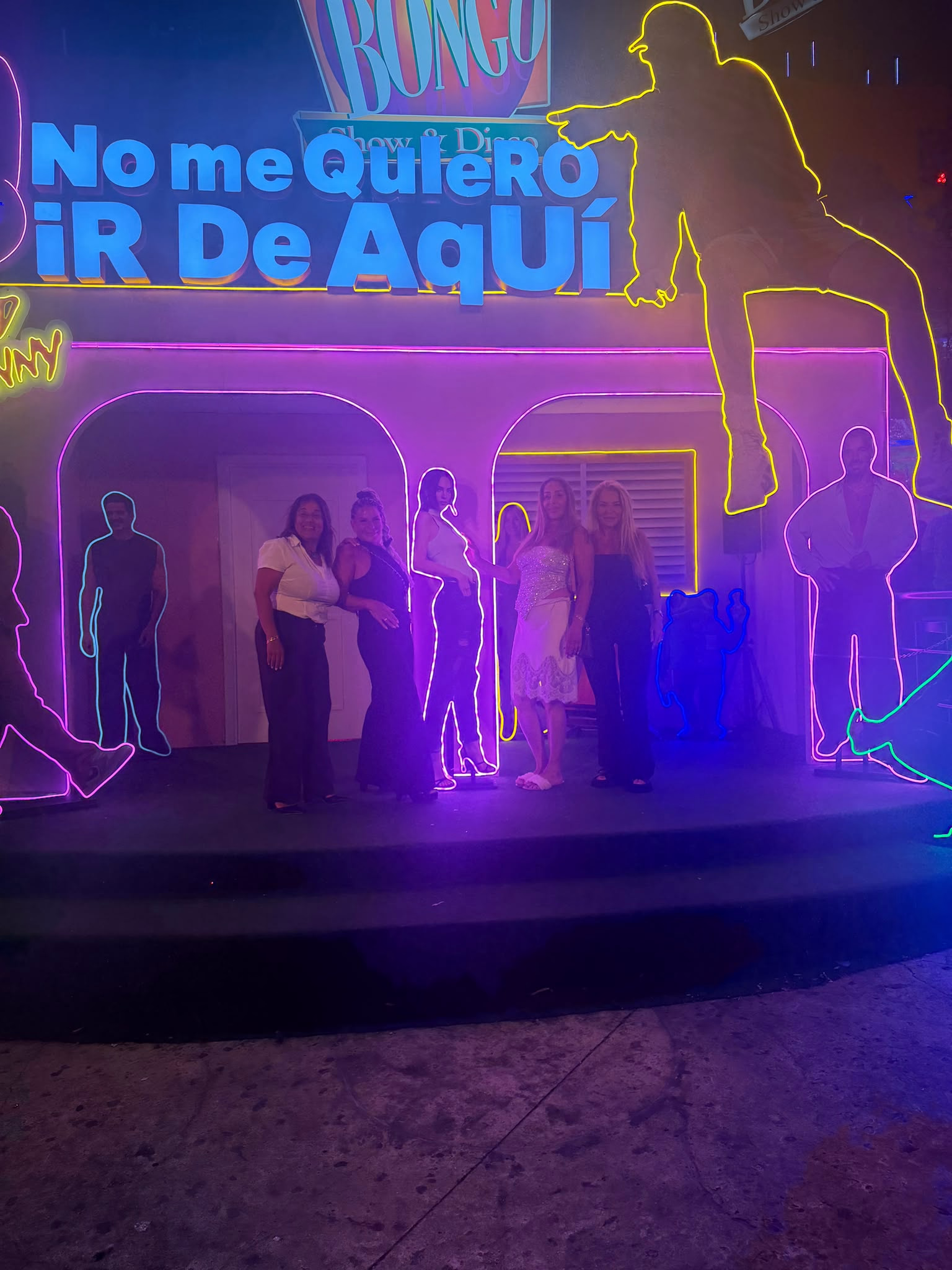 חופשה במקסיקו Members of Mrs. Simi A.'s group posing together beneath colorful neon artwork in Cancun